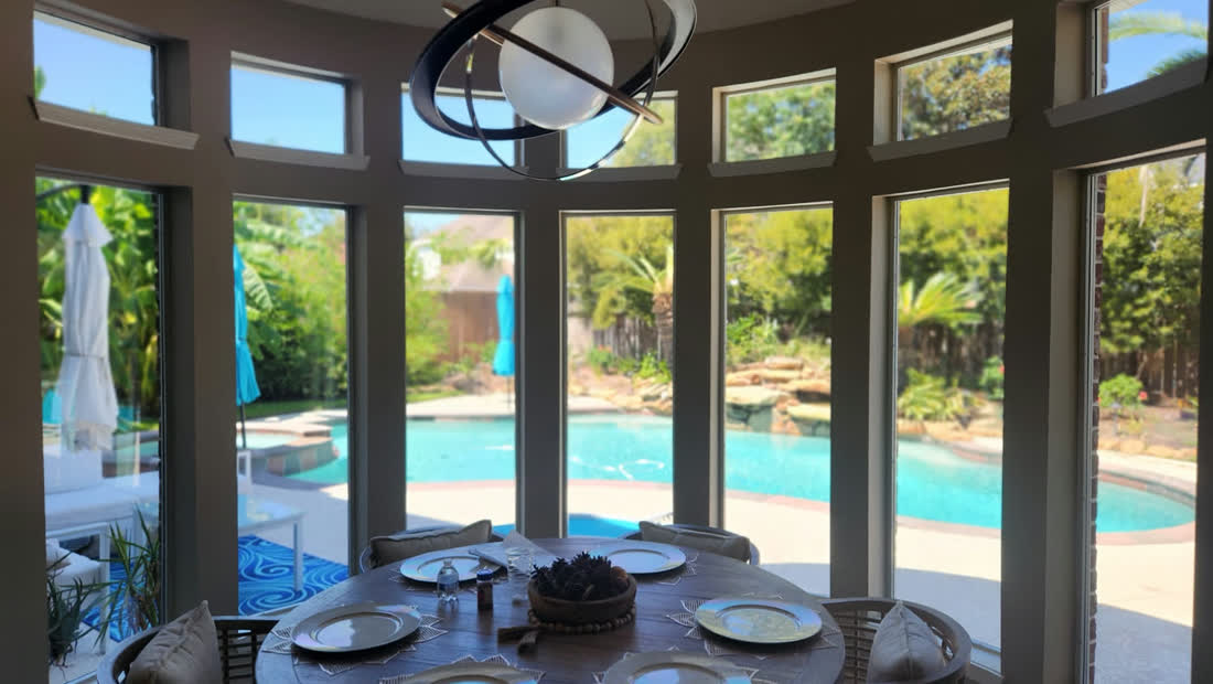 A sunroom with tinted windows looking out on a back yard pool