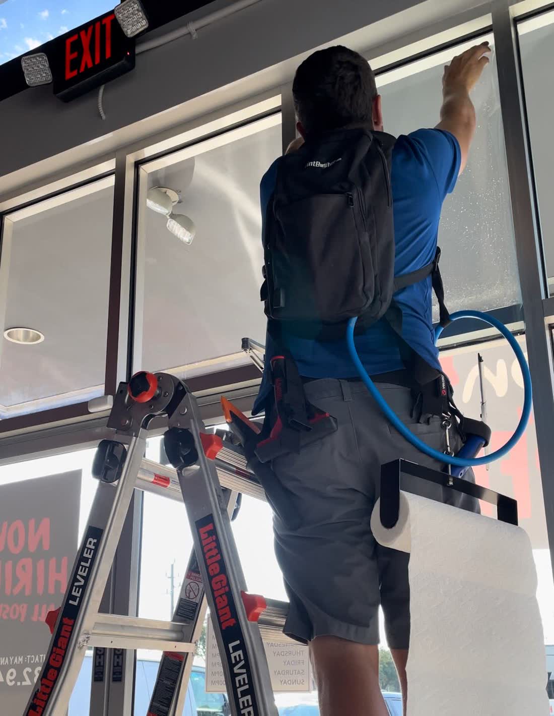 A Tint Days installer on a ladder tinting restaurant storefront glass