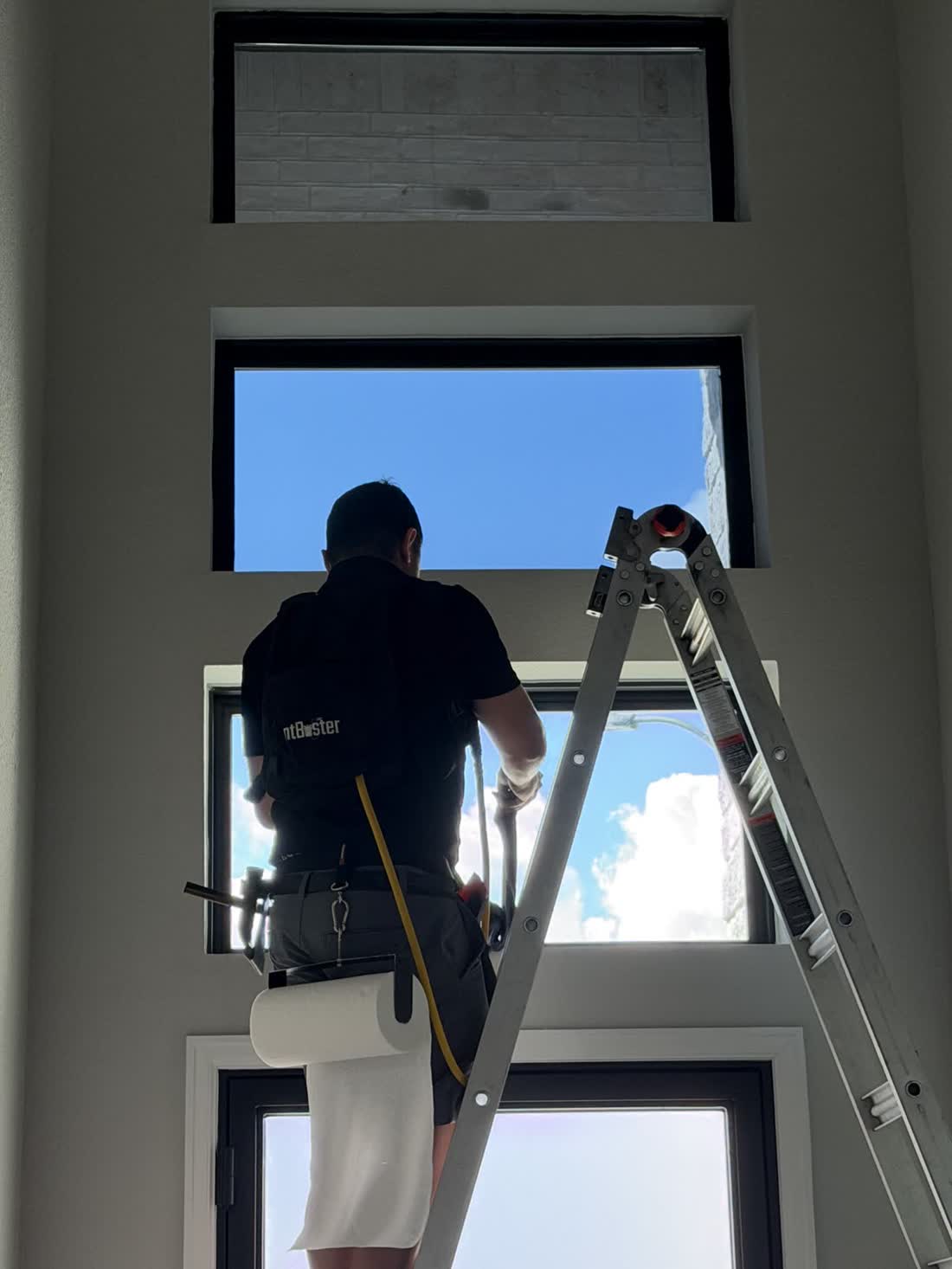 An installer on a ladder tinting a tall entry window