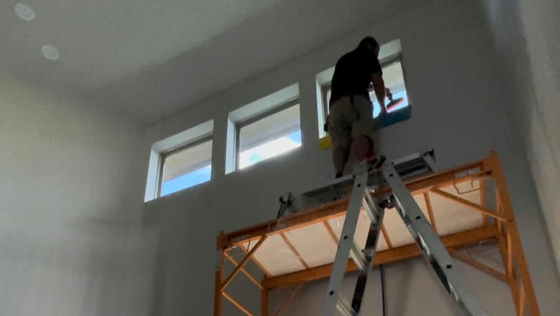 A Tint Days installer on a ladder fitting film to tall windows in a bright room