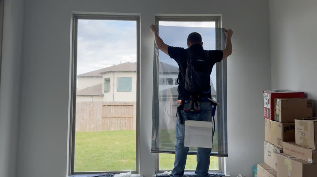 An installer smoothing film onto a tall window with the back yard visible through the glass